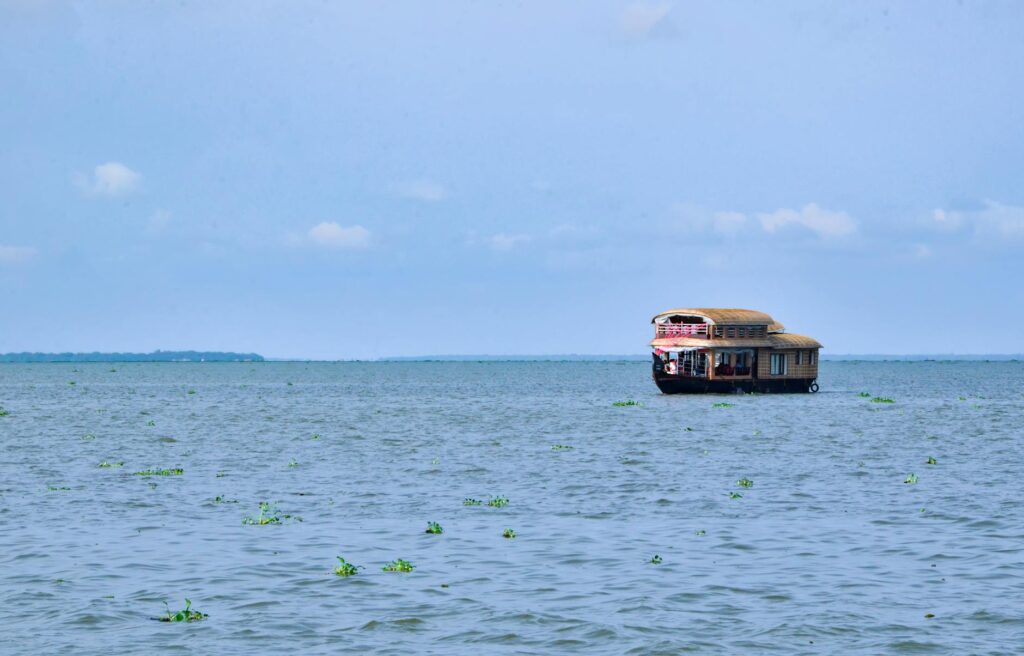 Traditional wooden Kerala backwaters houseboat gliding through calm palm-lined waterways in Kerala, India.