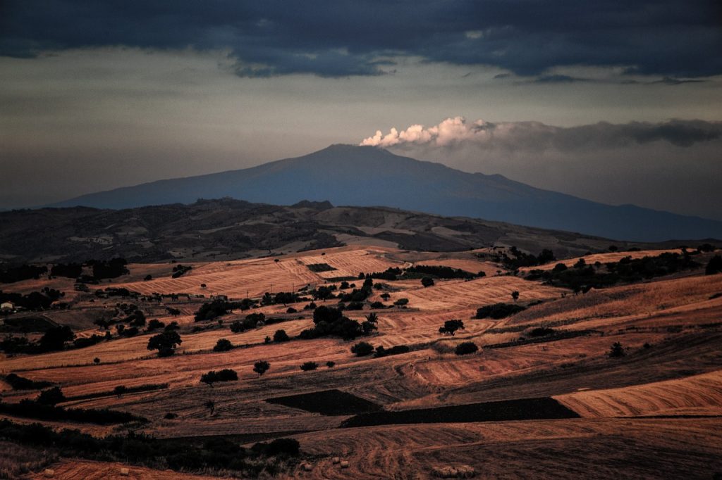 Mount Etna in the distance beyond harvested farmland in eastern Sicily, under storm clouds