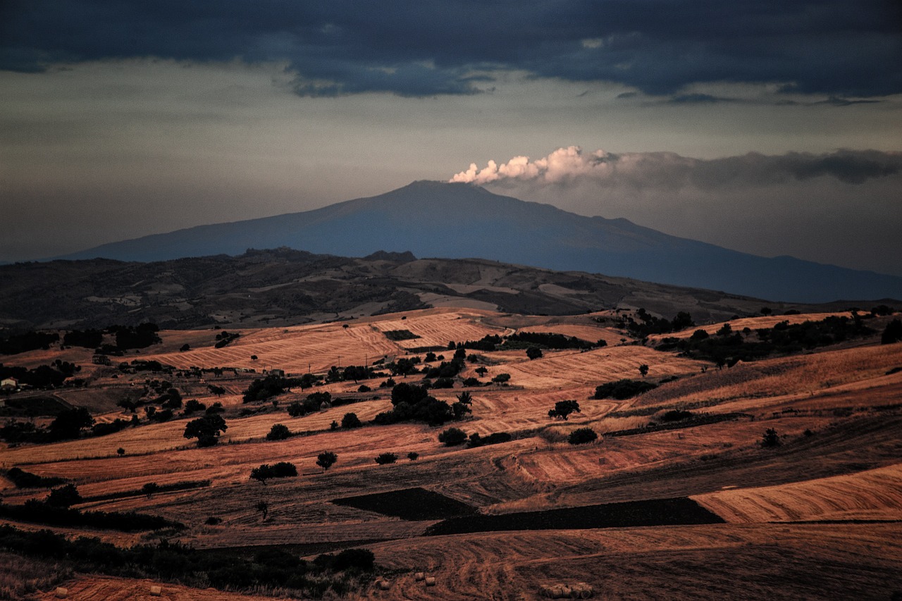 Mount Etna in the distance beyond harvested farmland in eastern Sicily, under storm clouds