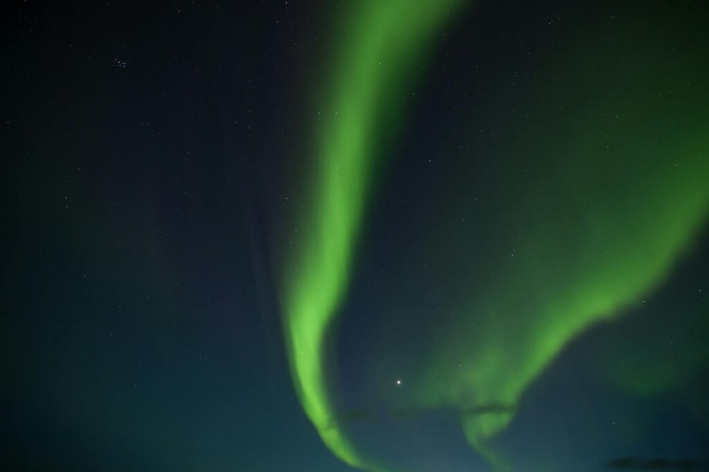 Vibrant green and purple northern lights dancing over a snow-covered Icelandic landscape at night.
