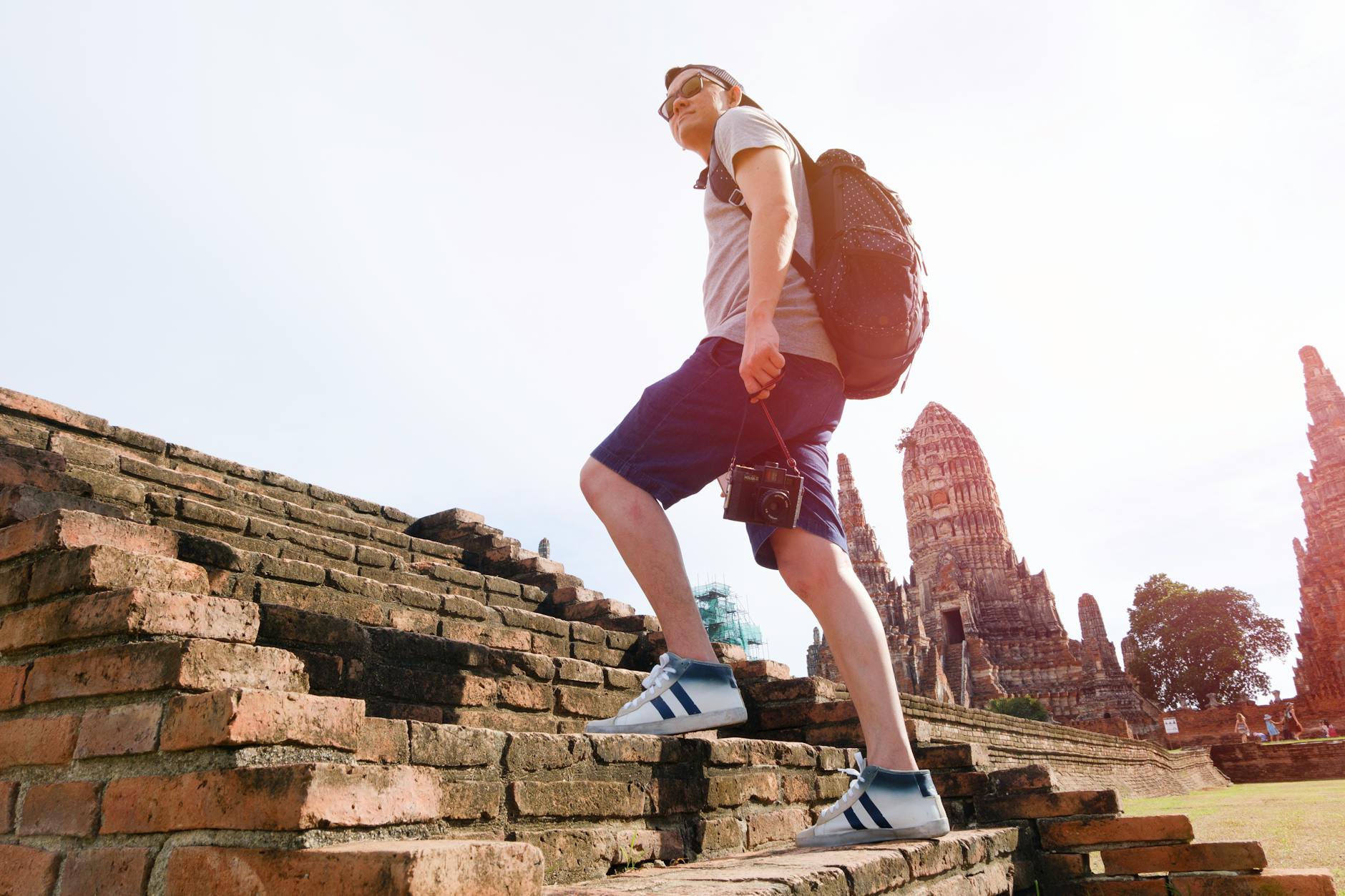 Solo traveler with backpack exploring a vibrant Thai temple street market at golden hour in Thailand.