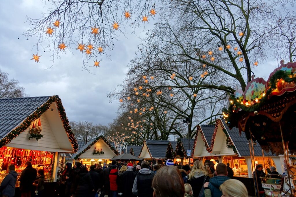 Crowds among festive stalls under hanging star lights at a Cologne Christmas market