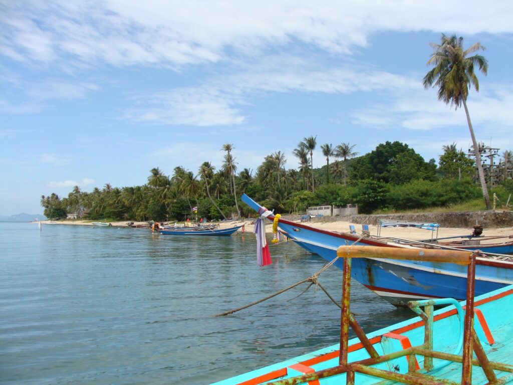 Longtail boats moored on a palm-fringed Koh Samui beach, Thailand, for comparing Koh Samui vs Phuket vs Koh Lanta