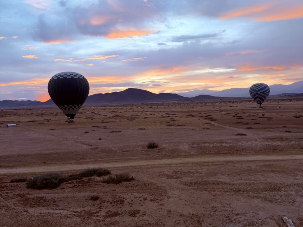 Hot-air balloons landing in the desert outside Marrakech at sunrise, with the Atlas foothills behind