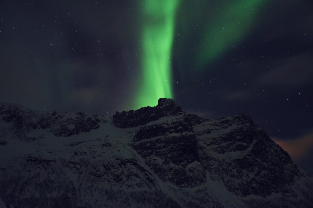 Green northern lights rising over snowy mountains near Tromsø, Norway